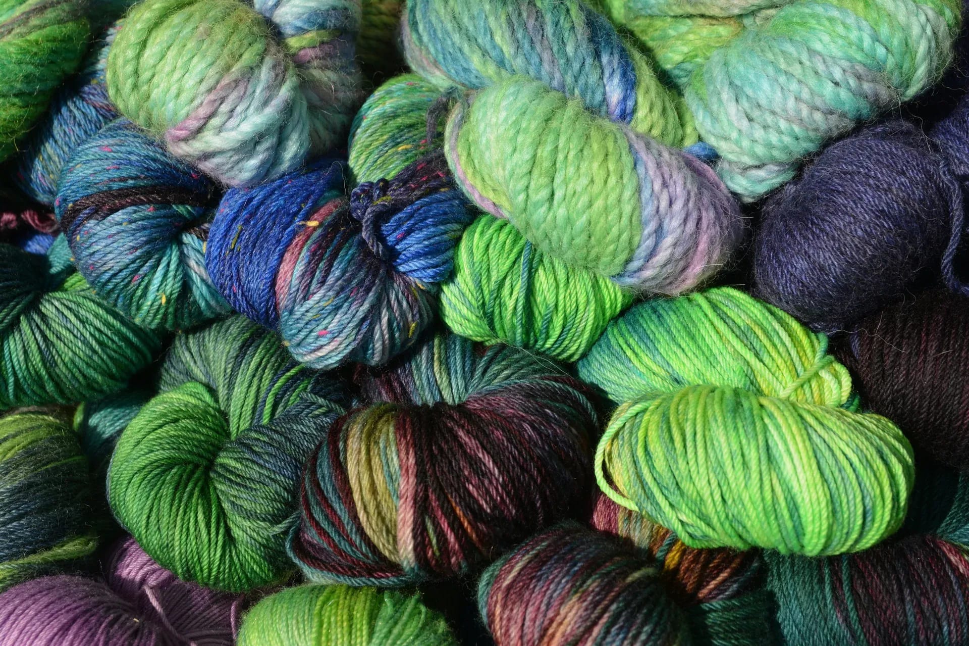 Pile of multicoloured wool skeins in shades of green, blue and purple